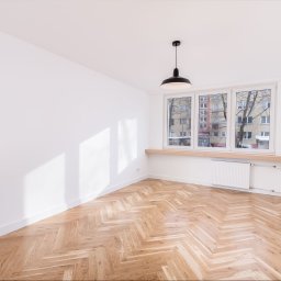 ARCHITEKTURA WNĘTRZ Jakub Tarnowski - Jasne, puste wnętrze z parkietem w jodełkę, białymi ścianami i oknem z widokiem na budynek. Czarna lampa wisząca dodaje kontrastu. Minimalistyczny design.