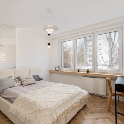 ARCHITEKTURA WNĘTRZ Jakub Tarnowski - Jasna sypialnia z łóżkiem, biurkiem i dużym oknem. Parkiet w jodełkę, minimalistyczne lampy i lustro tworzą przytulną, nowoczesną przestrzeń.