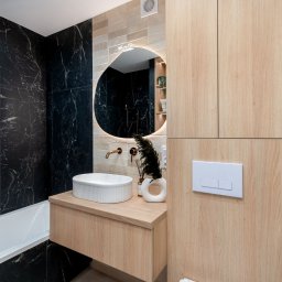 ARCHITEKTURA WNĘTRZ Jakub Tarnowski - Nowoczesna łazienka z czarnymi marmurowymi płytkami, okrągłym lustrem z podświetleniem LED i drewnianą szafką pod umywalką.