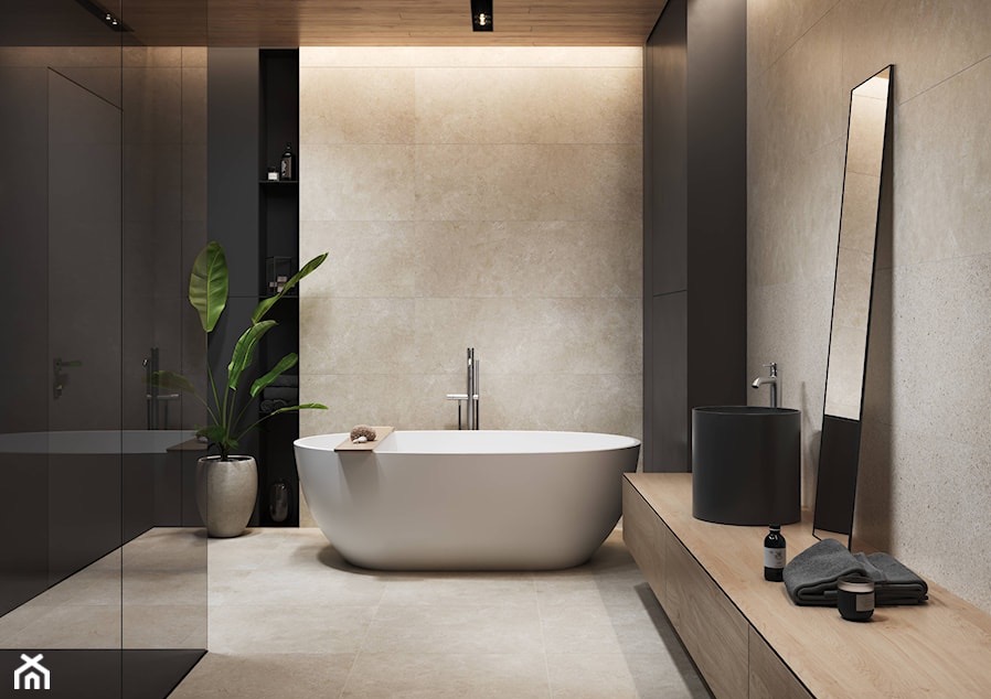Nowoczesna łazienka z wolnostojącą białą wanną, czarną umywalką nablatową, beżowymi płytkami i wysokim lustrem, oświetlona listwą LED, z rośliną w doniczce.