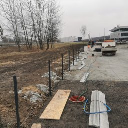 Drenaż Ogrodzenia Marek Chmielewski - Przygotowanie terenu pod budowę ogrodzenia: wbite słupki, rozciągnięty sznurek wyznaczający linię, ułożone krawężniki, widoczny właz kanalizacyjny i ciężarówka z piaskiem w tle.