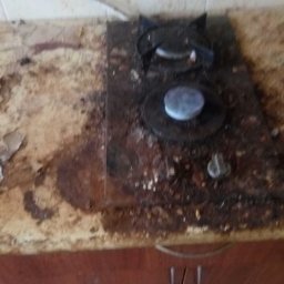 Natali Cleaning - Bardzo zabrudzona płyta kuchenna z dwoma palnikami na blacie z odchodzącą okleiną, widoczne resztki jedzenia i tłuszcz.