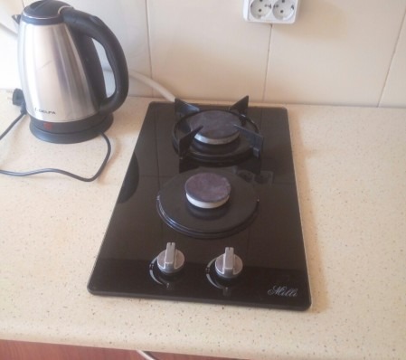 Czarna, dwupalnikowa płyta gazowa marki Hilli, zamontowana w jasnym blacie kuchennym, obok czajnika elektrycznego i gniazdka. Palniki przykryte, pokrętła w pozycji wyłączonej.