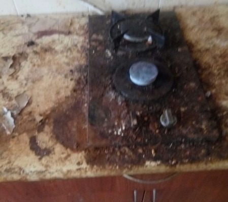 Bardzo zabrudzona płyta kuchenna z dwoma palnikami na blacie z odchodzącą okleiną, widoczne resztki jedzenia i tłuszcz.