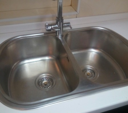 Dwukomorowy, stalowy zlew kuchenny z baterią, widoczne małe otwory przelewowe i odpływy z sitkami.