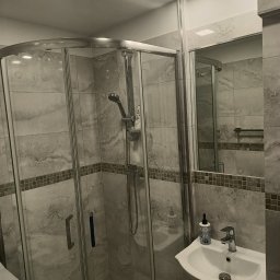 elmaro - Wykończona łazienka z kabiną prysznicową z zaokrąglonymi drzwiami, umywalką w szafce i szarymi płytkami imitującymi marmur z dekoracyjnym pasem na ścianach.