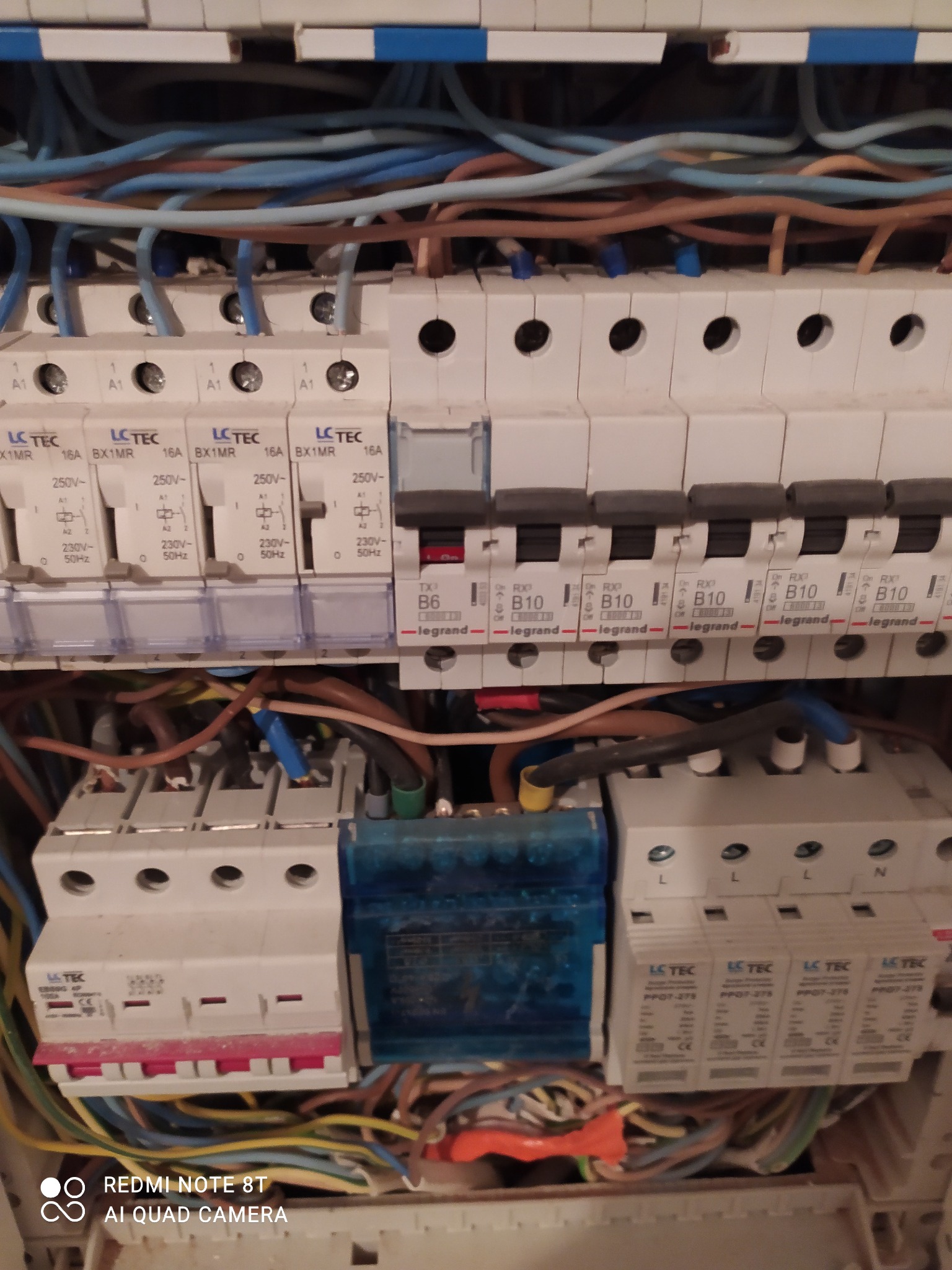 Otwarta skrzynka bezpiecznikowa z widocznymi przewodami, bezpiecznikami i wyłącznikami różnicowoprądowymi, zbliżenie na elementy instalacji elektrycznej wewnątrz szafki.