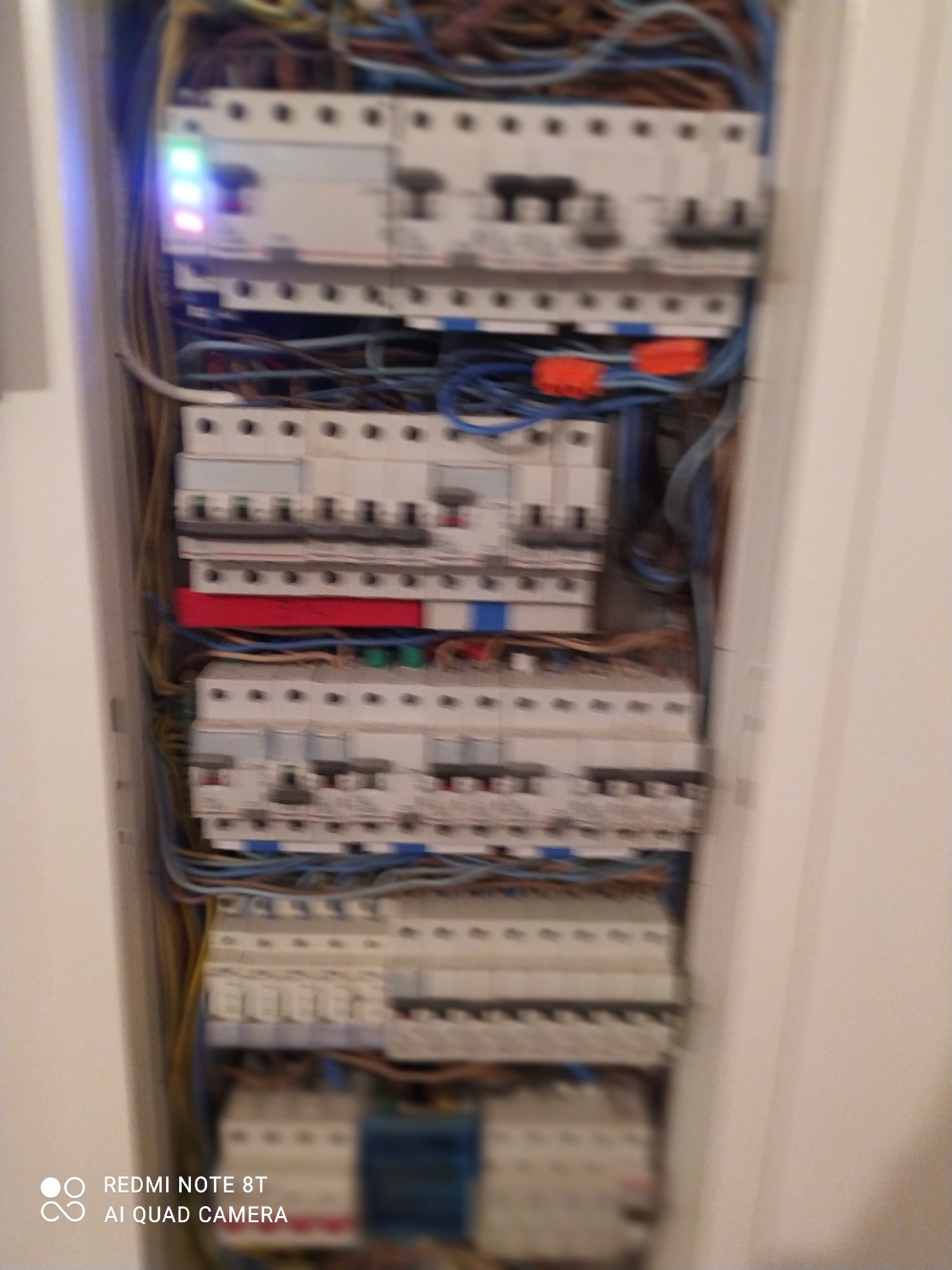 Rozdzielnica elektryczna z widocznymi bezpiecznikami, przewodami i elementami kontrolnymi, sfotografowana z bliska, z widocznym oświetleniem LED na jednym z modułów.