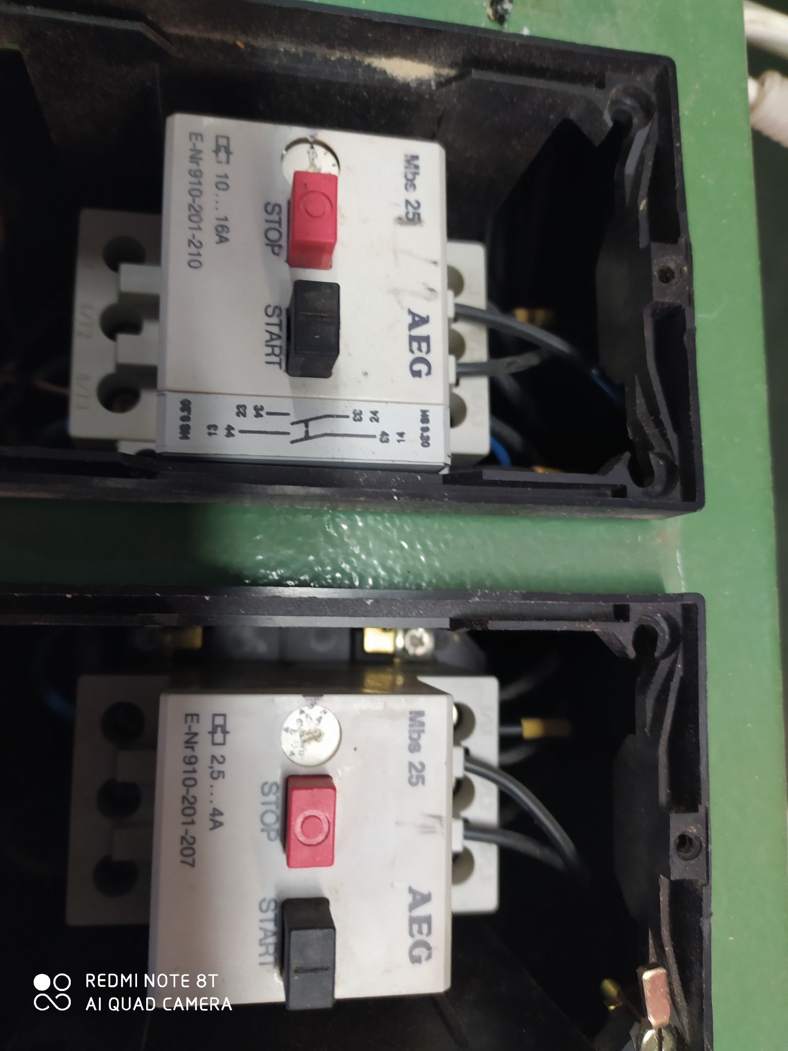 Dwa styczniki AEG Mbs 25 w czarnych obudowach, z przyciskami START/STOP, widoczne przewody elektryczne, obudowy lekko zakurzone.