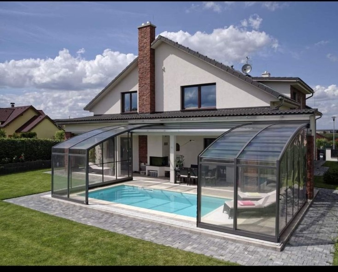 Zadaszony basen zewnętrzny z przesuwnymi szklanymi panelami, widok na dom z ceglanym kominem i zadbanym trawnikiem.