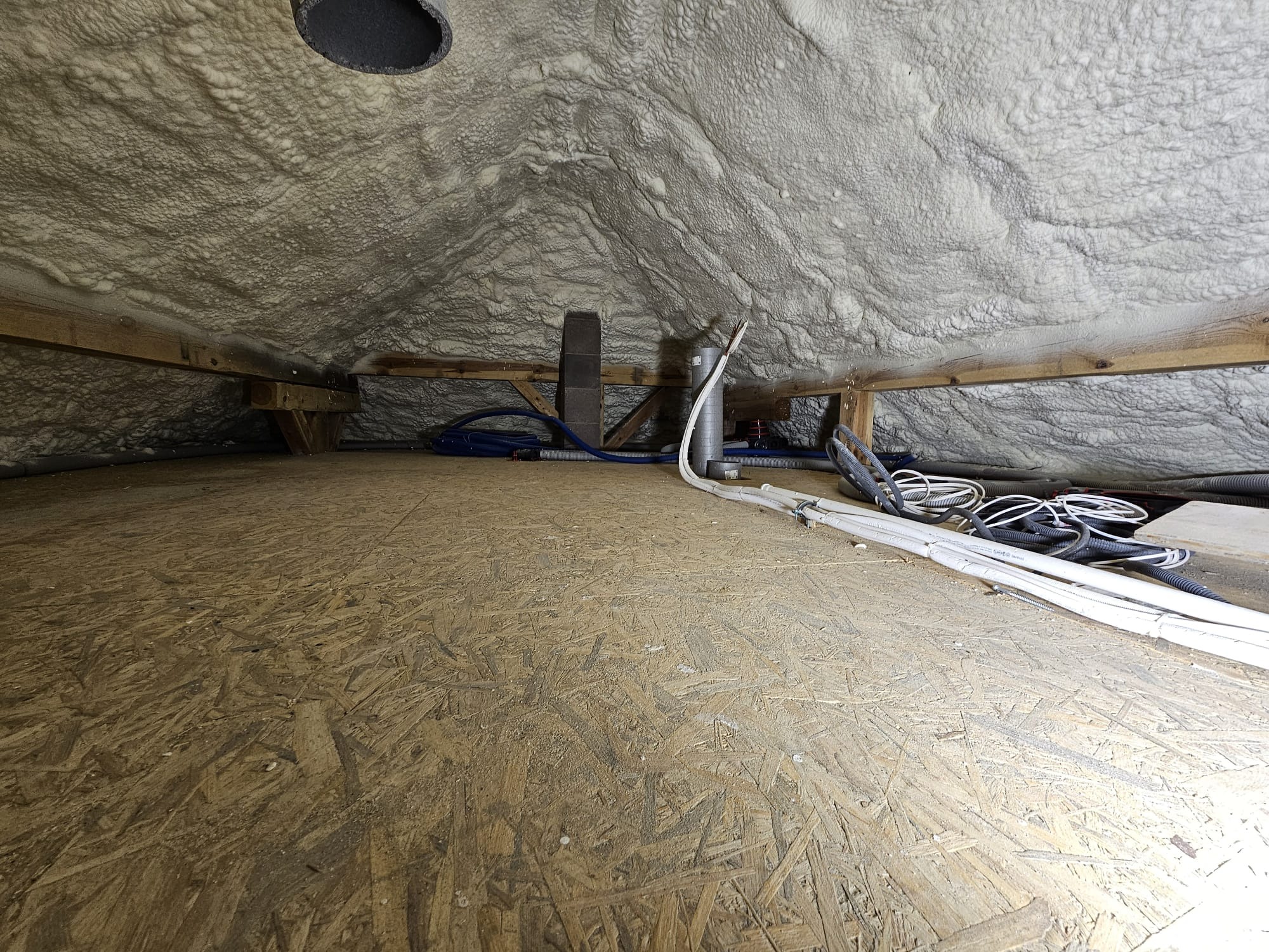 Poddasze z drewnianą konstrukcją i izolacją natryskową z pianki PUR, widoczne przewody instalacyjne i fragment podłogi z płyty OSB.