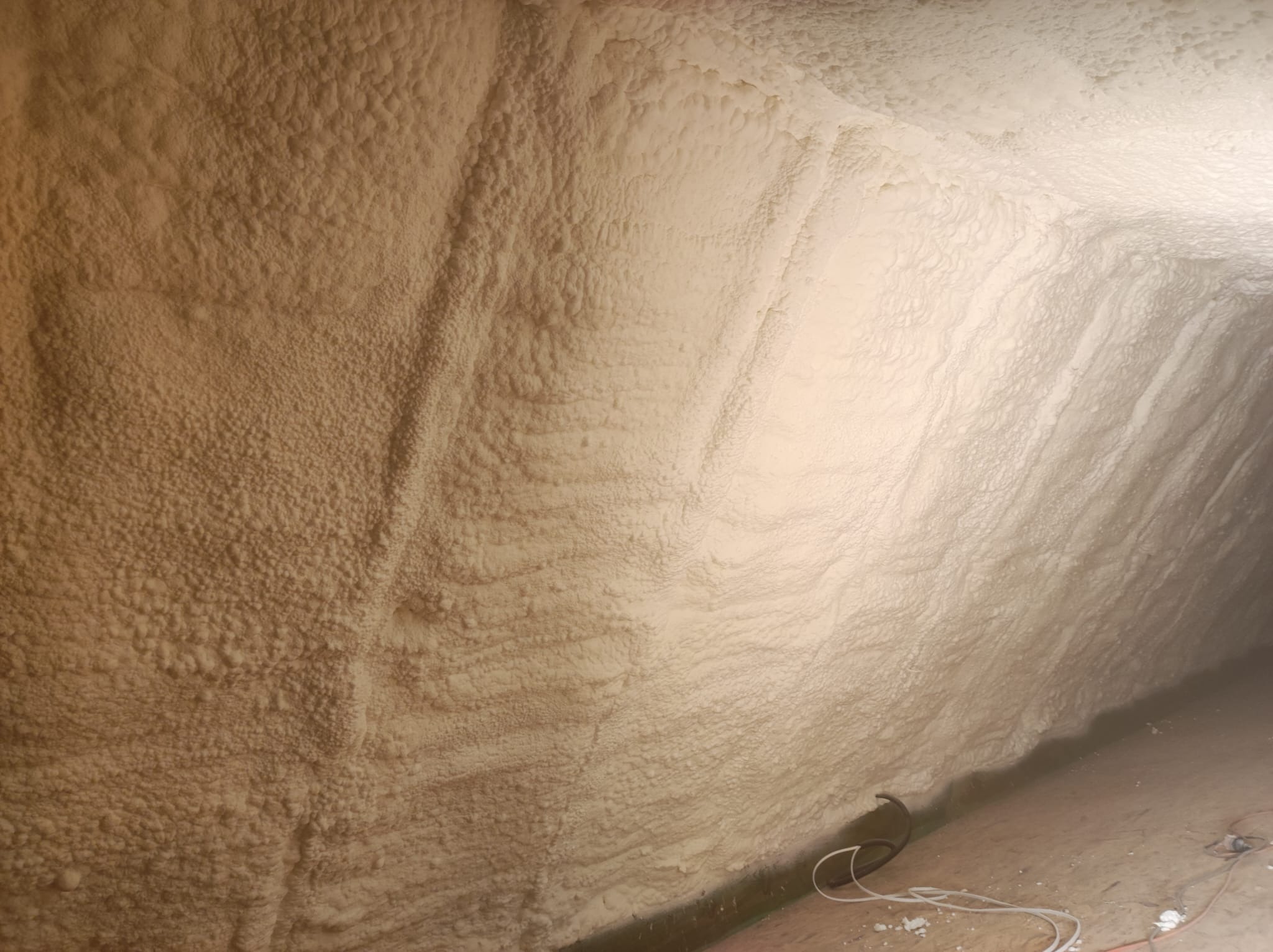 Poddasze po ociepleniu pianką PUR, widoczna struktura pianki o nierównej powierzchni, kabel na podłodze.