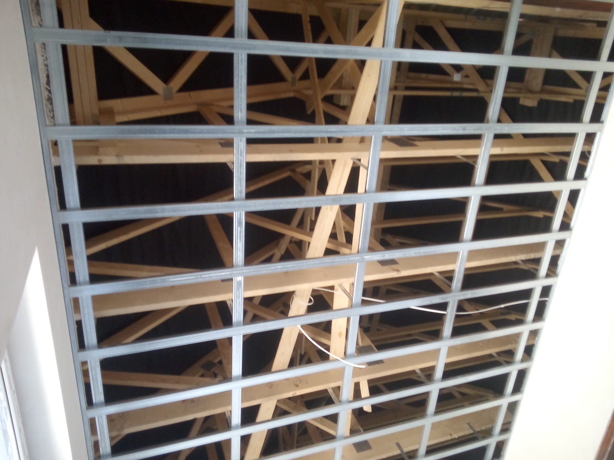 Metalowy stelaż sufitowy zamontowany na drewnianej konstrukcji dachu, widoczne przewody elektryczne.