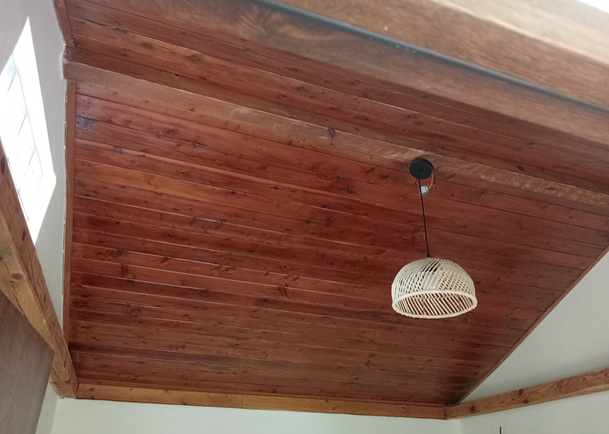 Drewniany sufit podbity boazerią w odcieniach czerwieni z widoczną lampą wiszącą z abażurem z wikliny