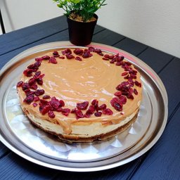 Bistro pełne smaków - Domowy sernik z polewą karmelową i żurawiną, podany na srebrnej tacy, obok doniczka z zieloną rośliną na ciemnym drewnianym stole.