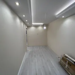 Wnętrze pokoju po remoncie, z położonymi jasnymi panelami podłogowymi, świeżo pomalowanymi ścianami w odcieniach beżu i białym sufitem z oświetleniem punktowym i dekoracyjnymi listwami.