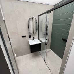Domer Dominik Stępień - Nowoczesna łazienka z szaro-beżowymi płytkami, czarną armaturą i kabiną prysznicową z zieloną ścianą z płytek strukturalnych.