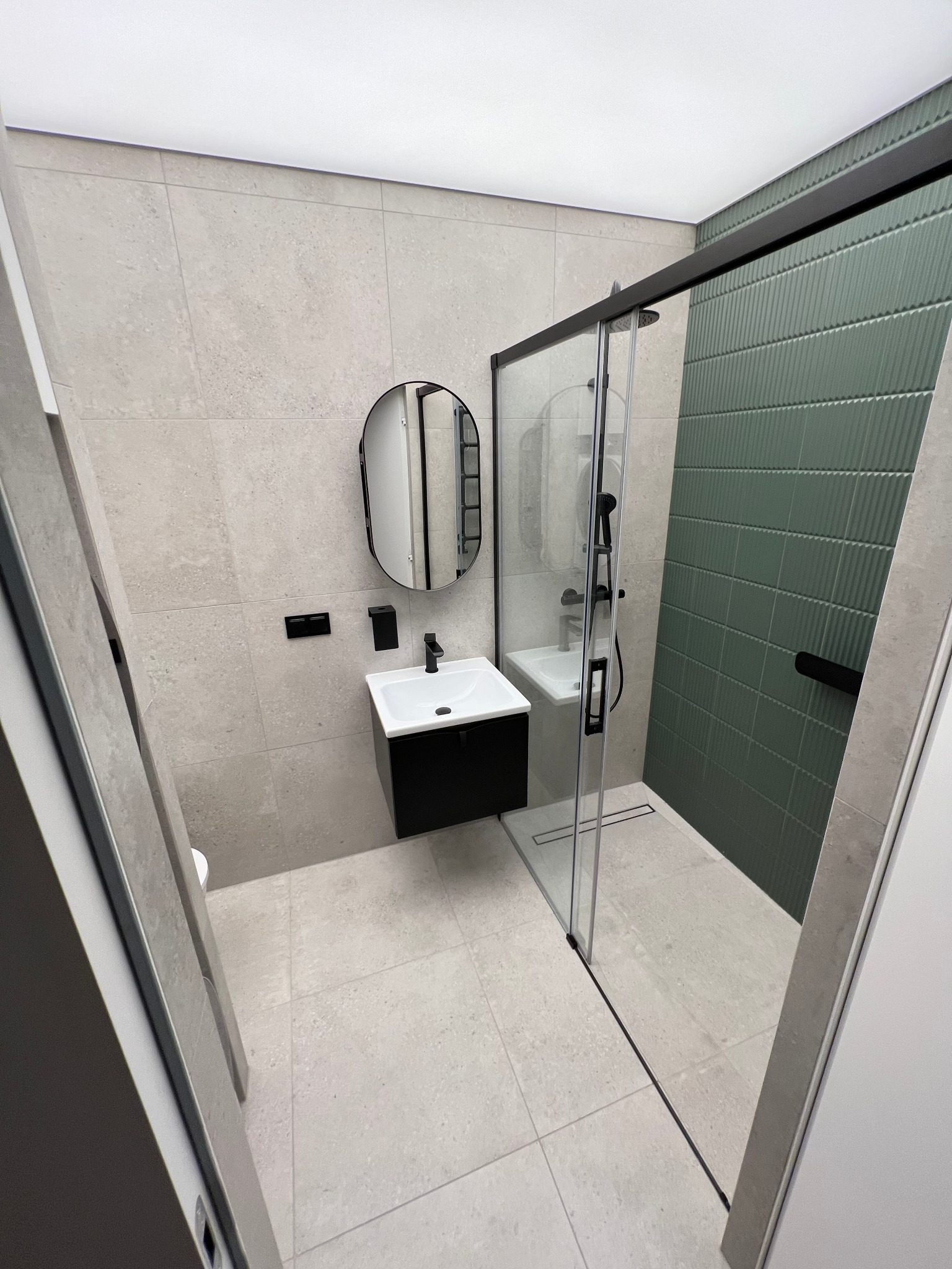 Nowoczesna łazienka z szaro-beżowymi płytkami, czarną armaturą i kabiną prysznicową z zieloną ścianą z płytek strukturalnych.