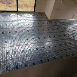 Hydroekipa. Specjaliści od mokrej roboty. - Instalacja ogrzewania podłogowego: rury grzewcze ułożone na folii aluminiowej z siatką, widok z góry, przygotowanie do zalania wylewką.