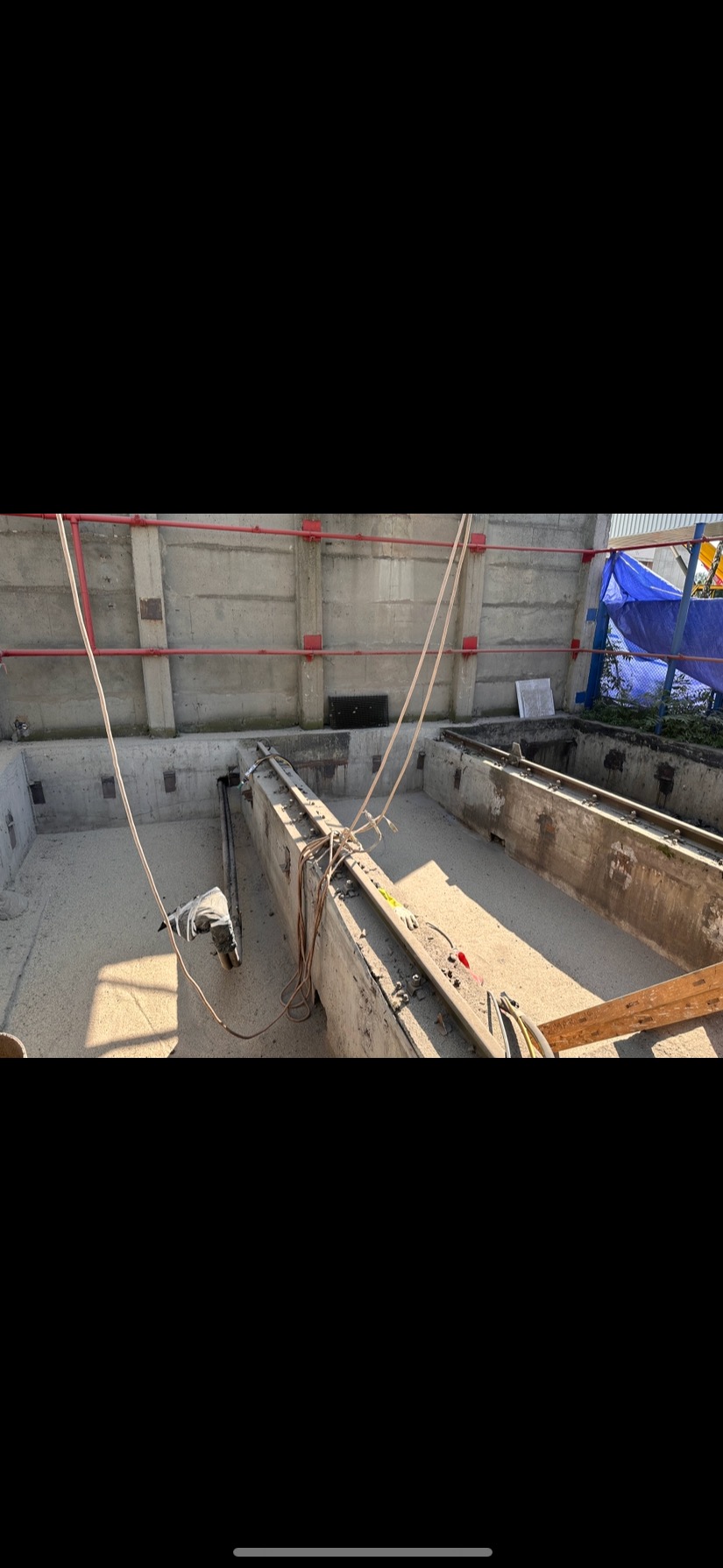 Betonowy zbiornik po piaskowaniu, widoczne zawieszone narzędzia i pozostałości piasku. Czerwone rury na ścianie, błękitna plandeka w tle.