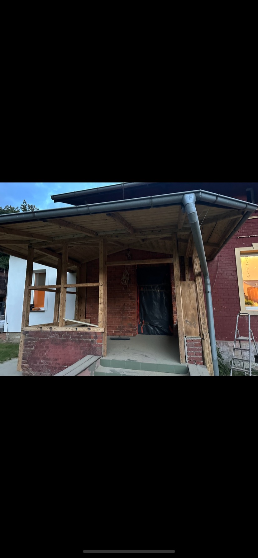Renowacja werandy domu z cegły: drewniana konstrukcja zadaszenia, przygotowana do dalszych prac wykończeniowych. Widoczne elementy instalacji rynnowej.