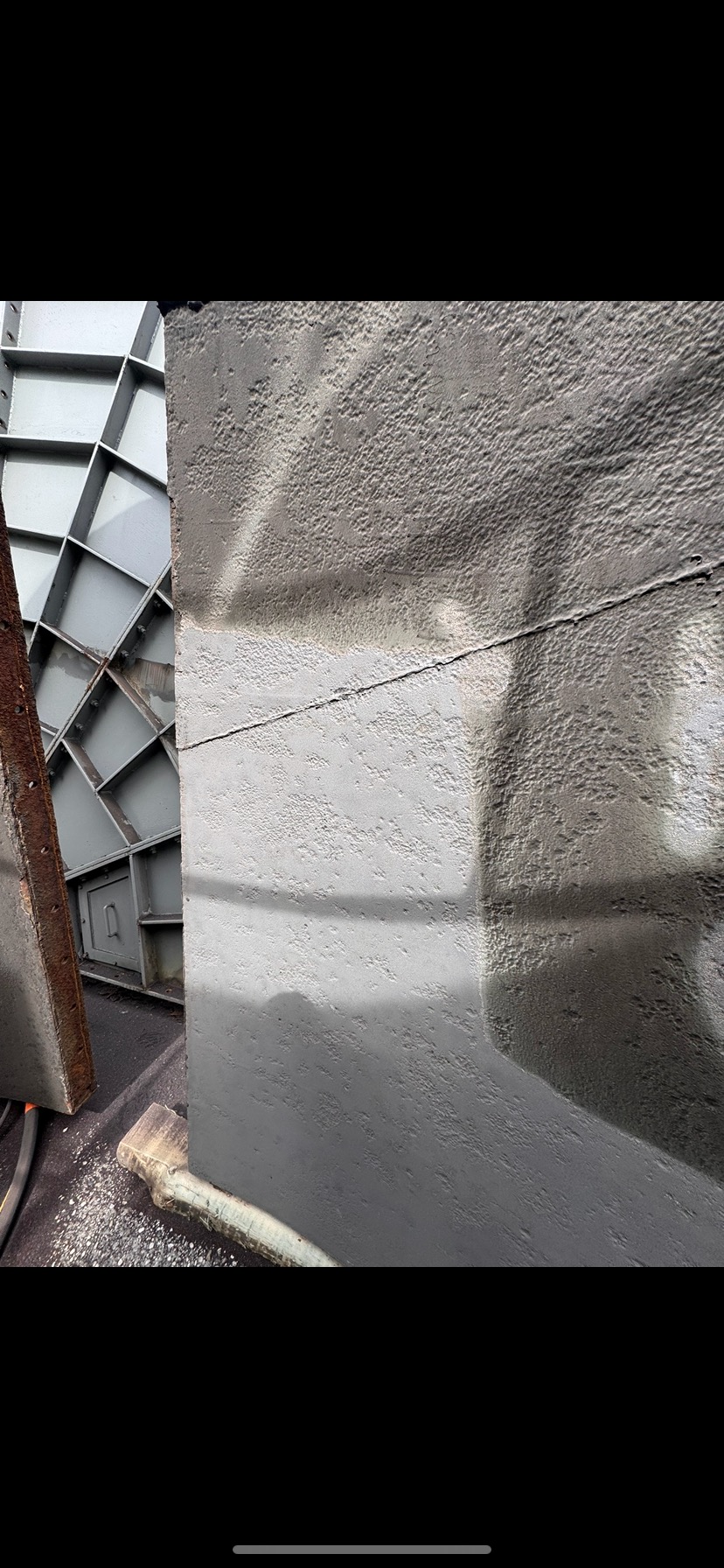 Szara, chropowata powierzchnia po piaskowaniu, z widocznymi elementami konstrukcji metalowej w tle i śladami wilgoci.