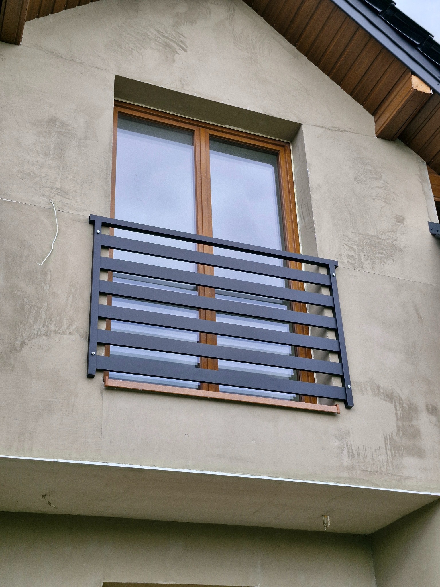 Czarna, pozioma balustrada metalowa zamontowana na zewnątrz okna na elewacji budynku w trakcie wykańczania.