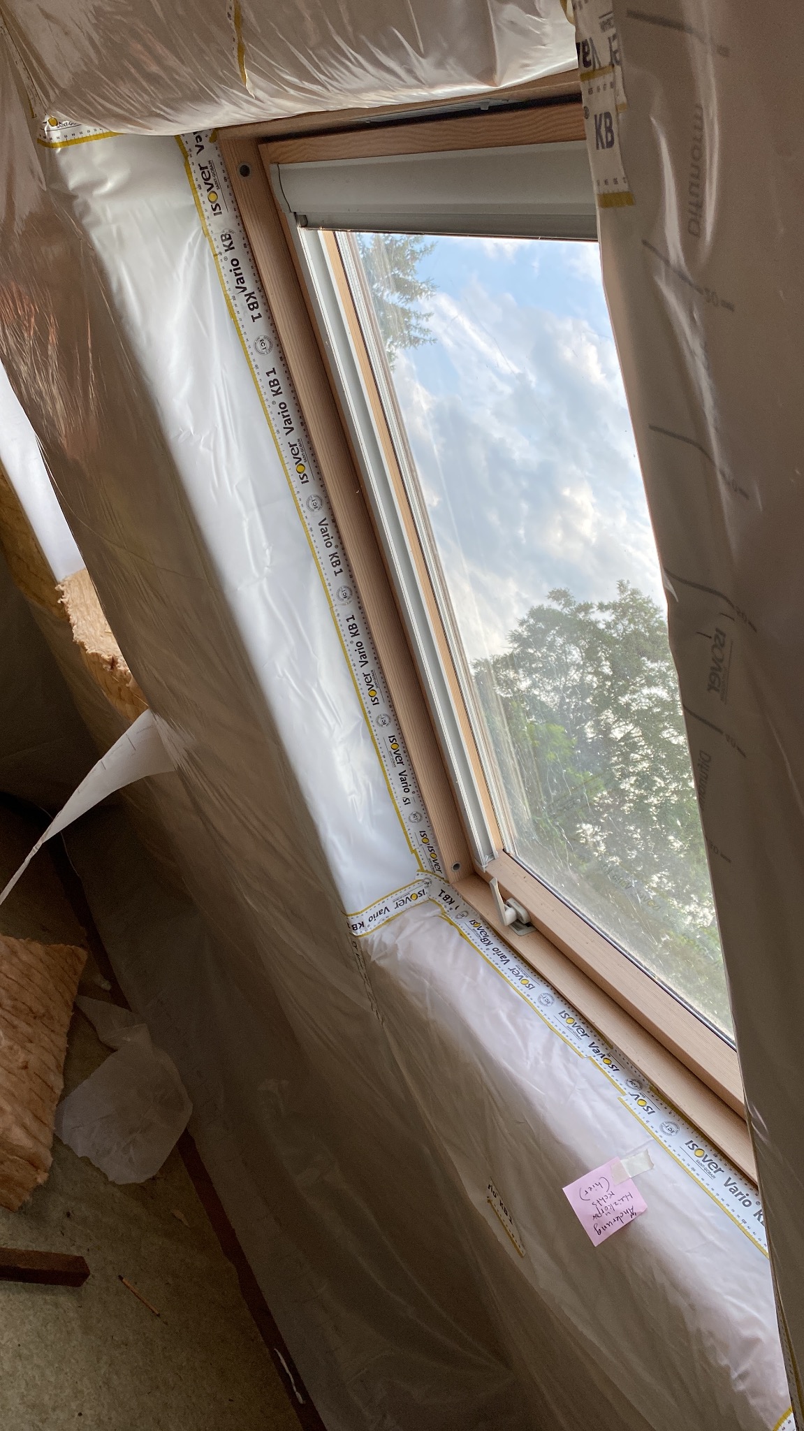 Poddasze z oknem dachowym w trakcie ocieplania, widoczna folia paroizolacyjna Isover Vario KB1 z notatką przyklejoną do folii.