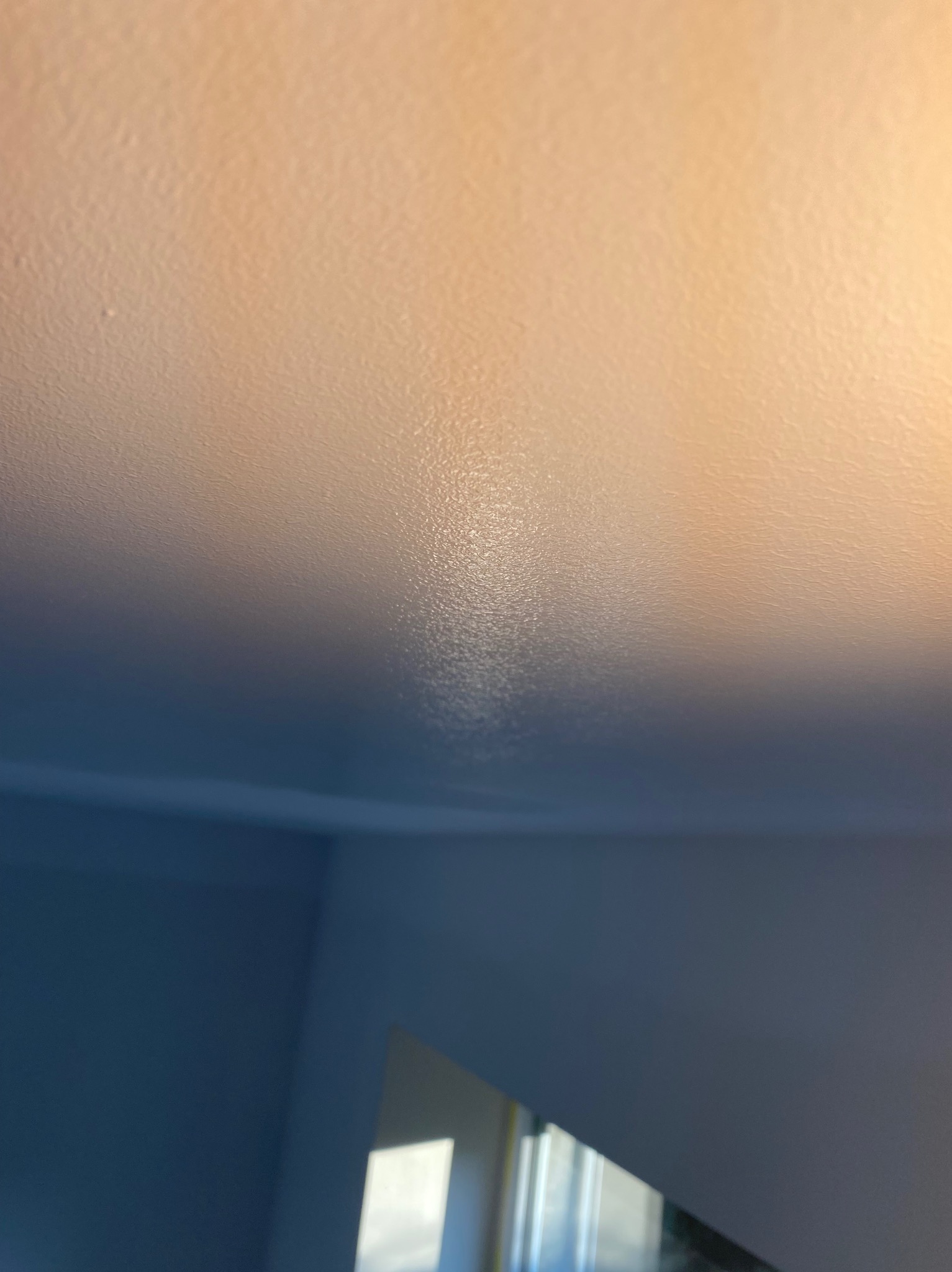 Pomarańczowo-biały sufit po gładziowaniu i malowaniu, widoczne przejście w niebieską ścianę w rogu pomieszczenia, oświetlone z góry.