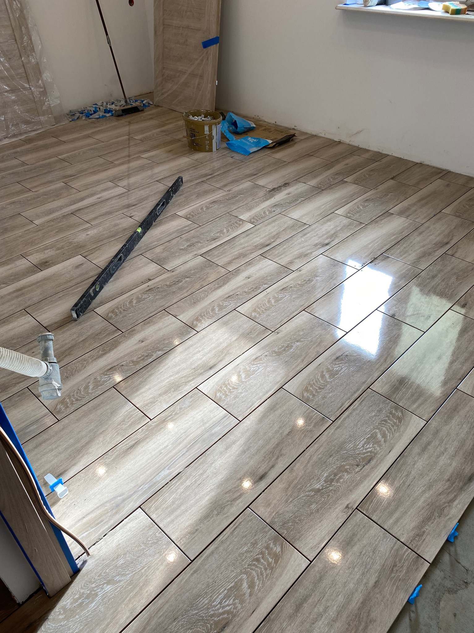 Ułożone, błyszczące płytki podłogowe imitujące drewno, poziomica i elementy montażowe widoczne na powierzchni, przygotowane do fugowania.