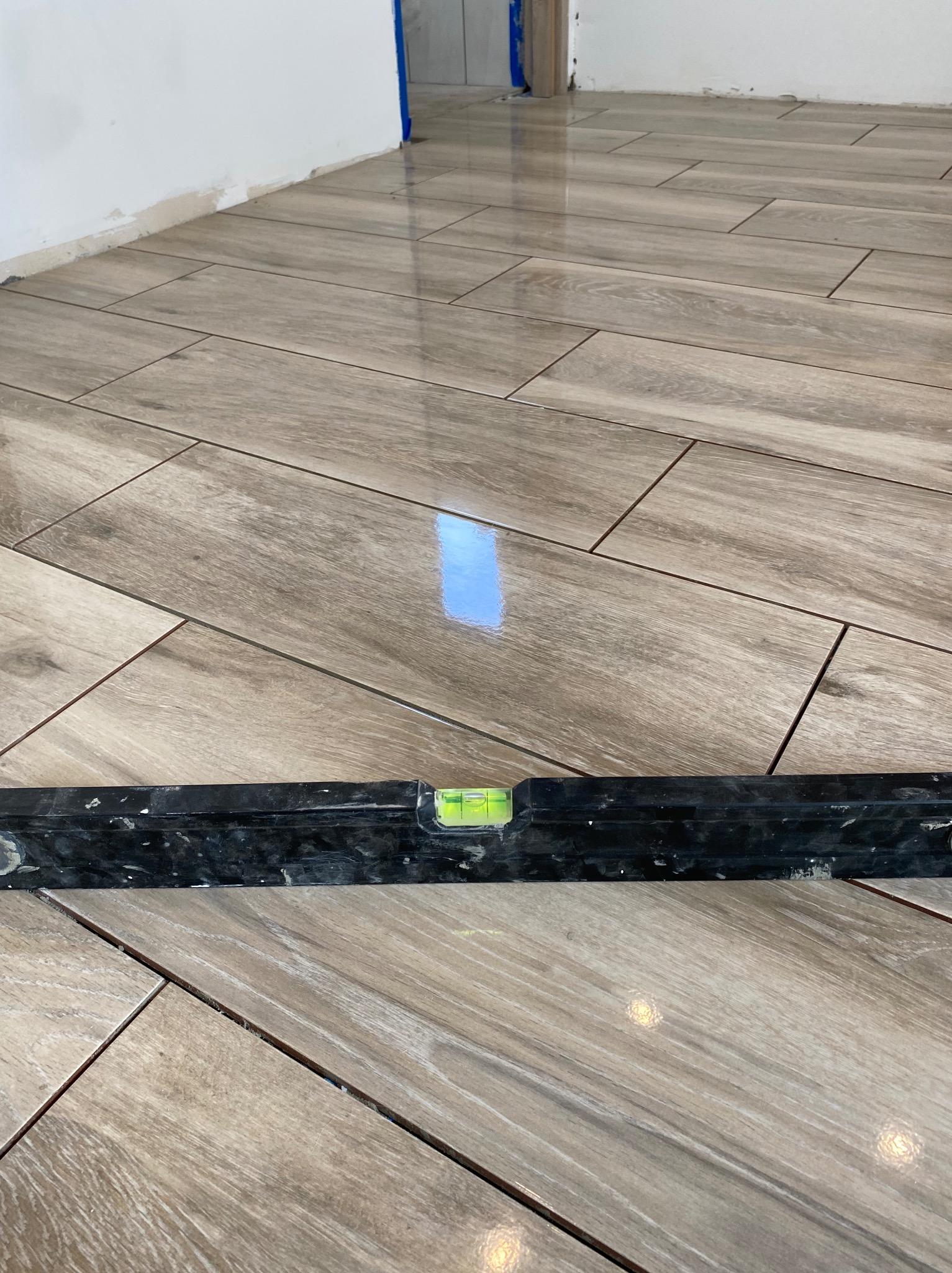 Ułożone, brązowe panele podłogowe imitujące drewno, sprawdzane poziomicą. Widoczne drobne niedoskonałości przy ścianie oraz odblask światła na powierzchni paneli.