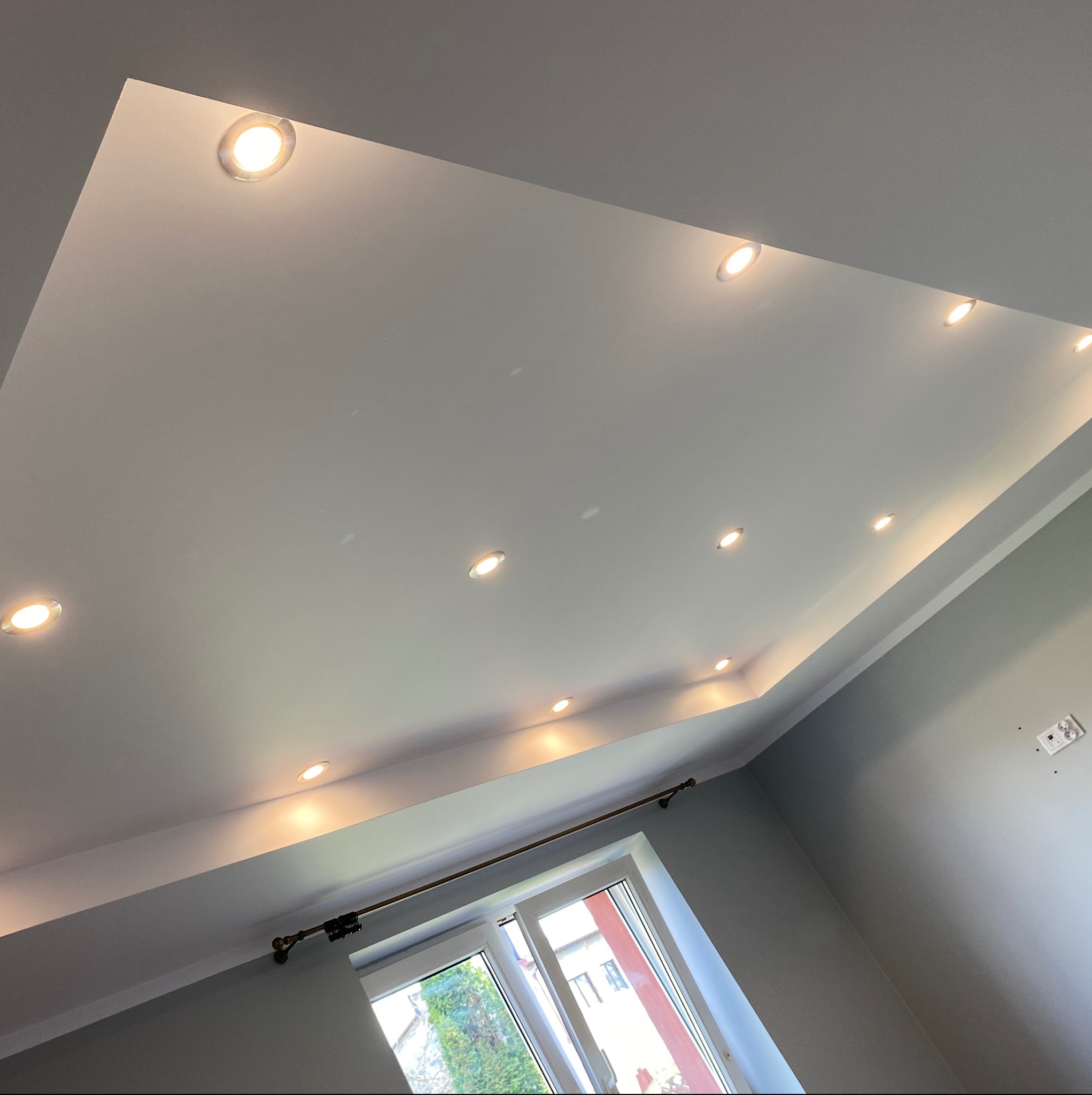 Nowoczesny sufit podwieszany z oświetleniem punktowym w kształcie prostokąta, świeżo po montażu w Jaworznie, widok z dołu na okno i karnisz.