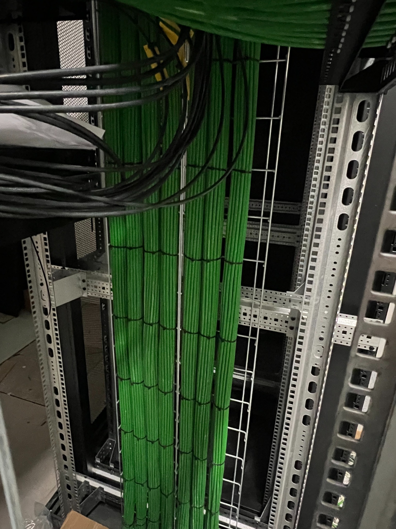 Uporządkowane kable w szafie serwerowej, przewody zielone spięte opaskami, widoczne elementy konstrukcyjne szafy rack, czarne kable u góry kadru.