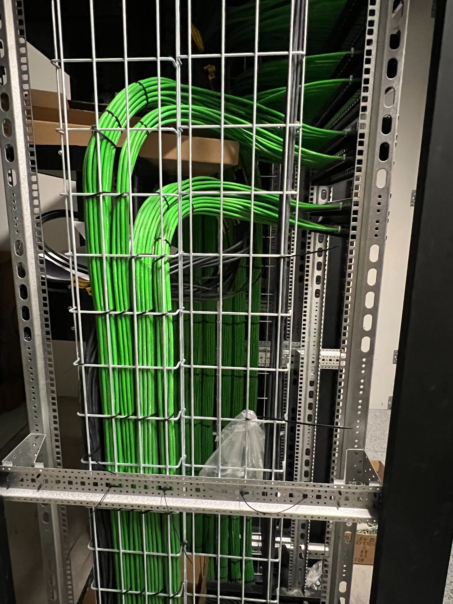Uporządkowane, zielone kable w metalowej szafie serwerowej. Estetyczne prowadzenie przewodów w centrum danych. Widoczne elementy montażowe i konstrukcja szafy.