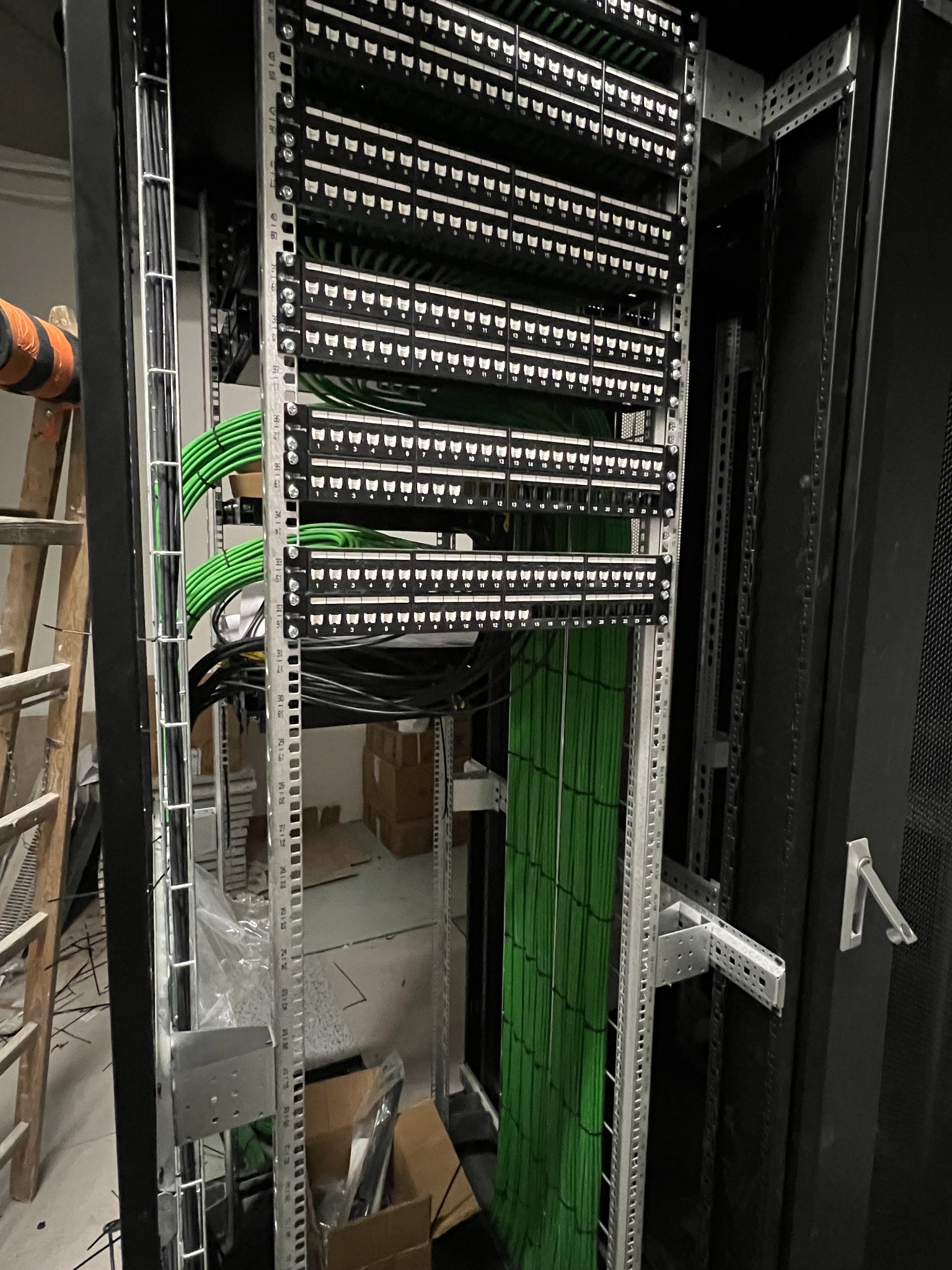 Panel krosowniczy z uporządkowanymi kablami w szafie rack, widoczne oznaczenia portów i drabinka kablowa. Elementy instalacji sieciowej w serwerowni.