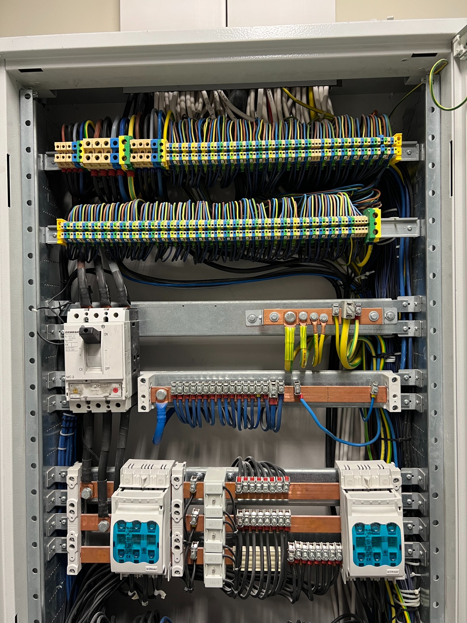 Rozdzielnia elektryczna z precyzyjnie ułożonymi kablami, listwami zaciskowymi i zabezpieczeniami. Widoczne przewody w różnych kolorach i elementy miedziane.