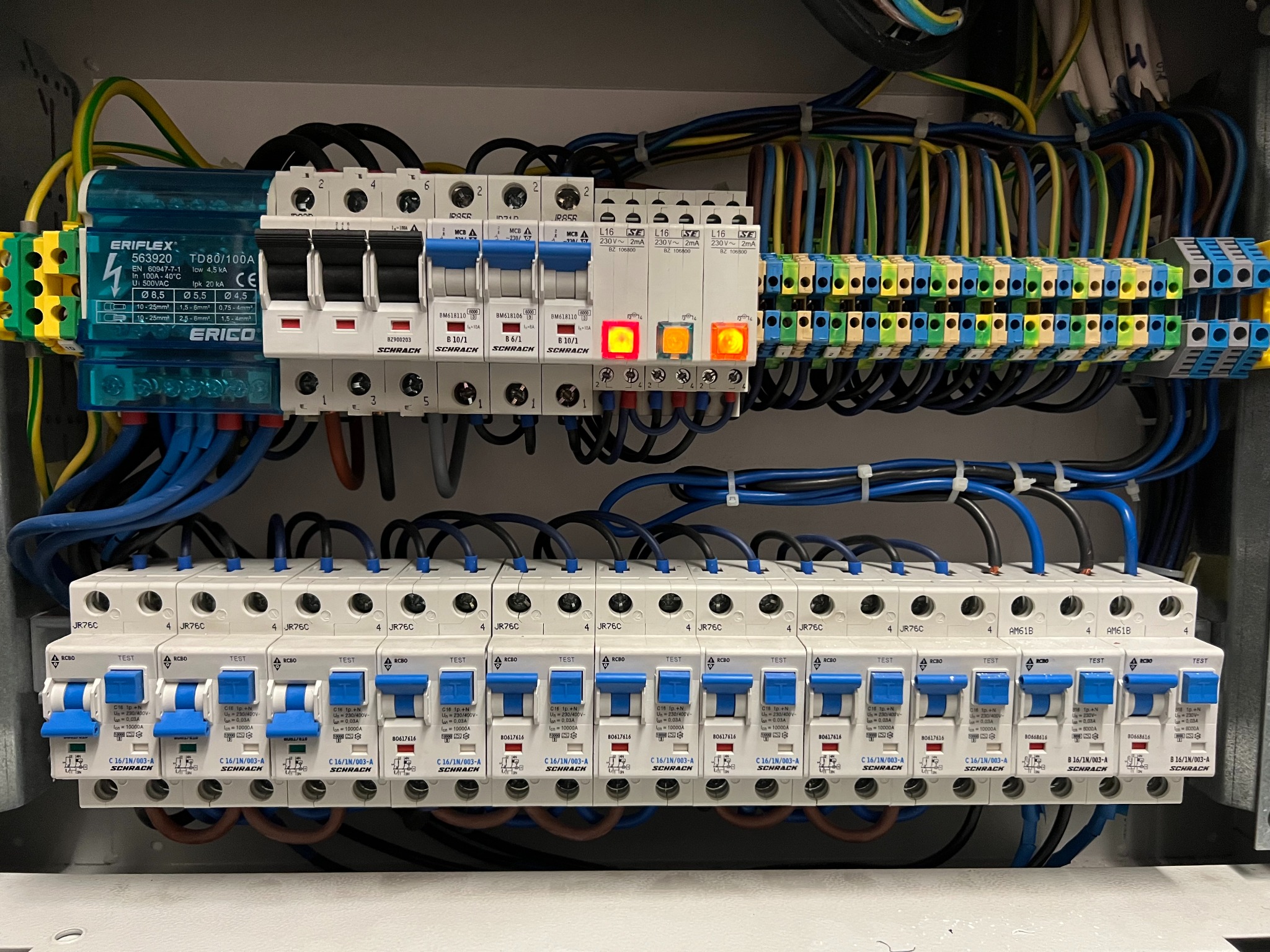 Rozdzielnica elektryczna z bezpiecznikami i przewodami, zainstalowana w Warszawie. Widoczne elementy instalacji elektrycznej i zabezpieczenia obwodów.