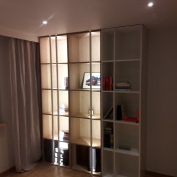 arkadia arkadiusz bialobrzewski - Regał modułowy z otwartymi półkami, część drewniana z oświetleniem wewnętrznym, część biała, ustawiony w rogu pokoju z parkietem i zasłoniętym oknem.