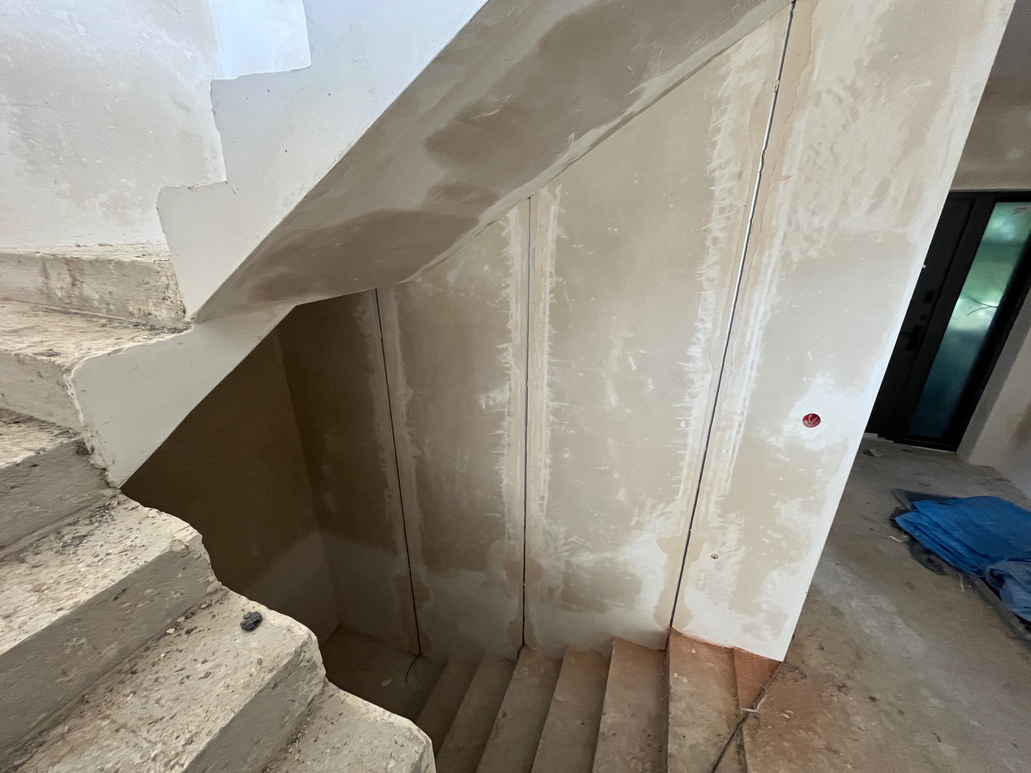 Surowe betonowe schody w trakcie wykańczania, widoczne pionowe kanały instalacyjne w ścianie, przygotowane pod okablowanie, z widoczną puszką instalacyjną.