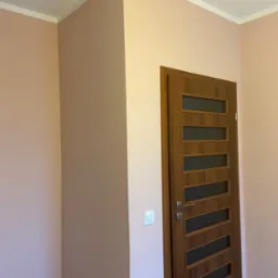 Świeżo pomalowane wnętrze z drzwiami wewnętrznymi z przeszkleniami, widoczna puszka z farbą w rogu pomieszczenia.