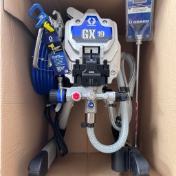 Silesia Vision Mateusz Drzazgowski - Nowy, nierozpakowany agregat malarski Graco GX19 w kartonowym pudełku, z akcesoriami i instrukcją. Sprzęt gotowy do użycia w pracach malarskich.