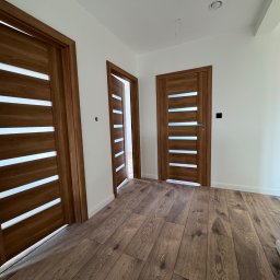 Silesia Vision Mateusz Drzazgowski - Nowoczesne, drewniane drzwi z przeszkleniami w Chorzowie, zamontowane w jasnym wnętrzu z drewnianą podłogą. Widoczne trzy skrzydła drzwiowe.