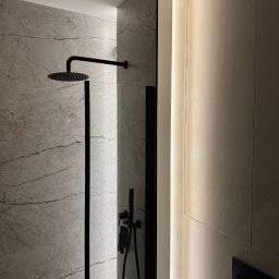 Silesia Vision Mateusz Drzazgowski - Nowoczesna kabina prysznicowa z deszczownicą i szklaną ścianką, podświetlona listwa LED. Marmurowe płytki i czarna armatura.