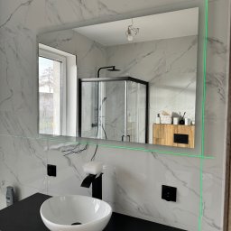 Silesia Vision Mateusz Drzazgowski - Nowoczesna łazienka z białymi płytkami imitującymi marmur, czarną armaturą i podświetlanym lustrem, ustawionym za pomocą lasera krzyżowego.