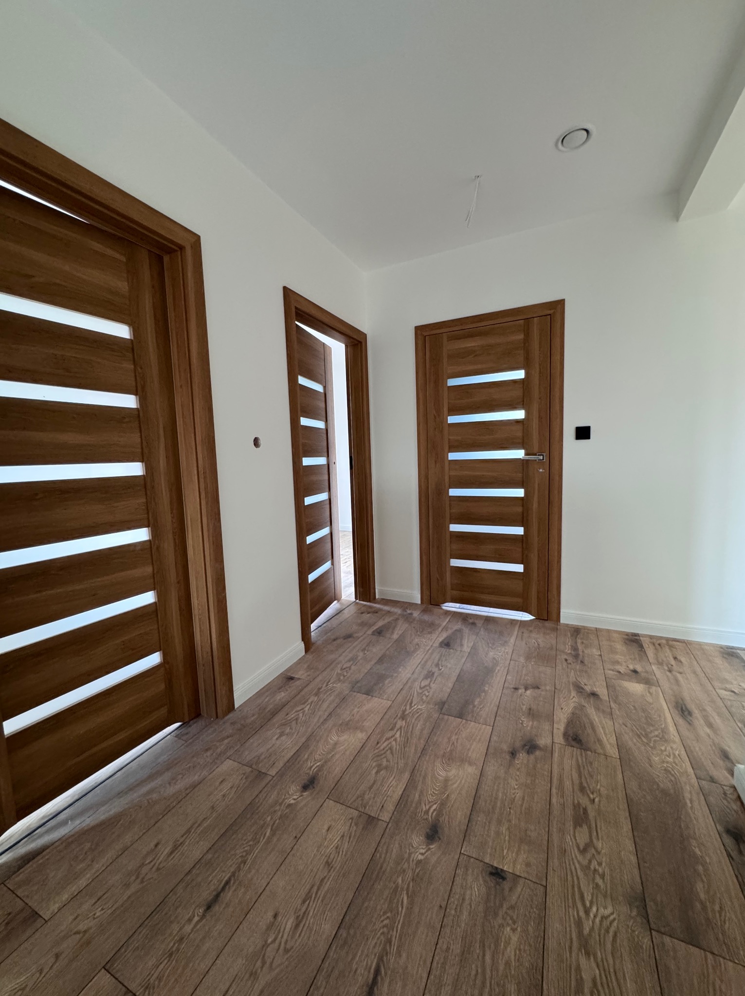 Nowoczesne, drewniane drzwi z przeszkleniami w Chorzowie, zamontowane w jasnym wnętrzu z drewnianą podłogą. Widoczne trzy skrzydła drzwiowe.