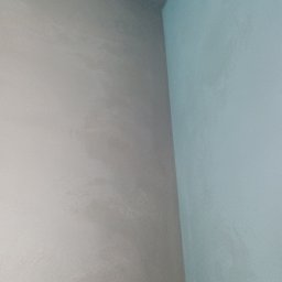 Przemysław Kuras PRZEM-BUD - Ściana wewnętrzna wykończona tynkiem maszynowym w odcieniach szarości i błękitu, widok na narożnik. Delikatna faktura tynku.