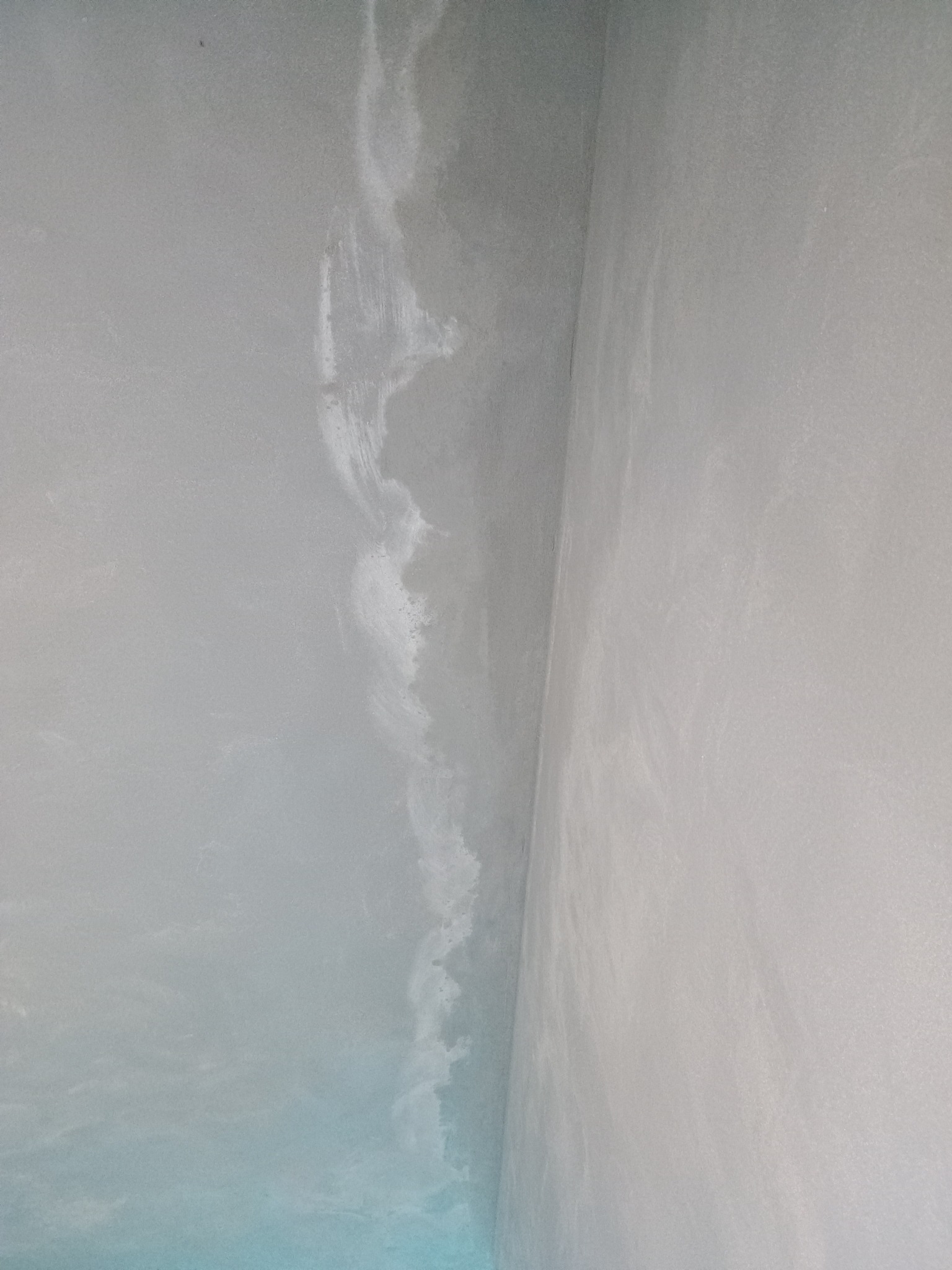 Świeżo nałożona, jeszcze mokra, gładź szpachlowa na ścianie w rogu pomieszczenia, widoczne ślady po szpachelce.