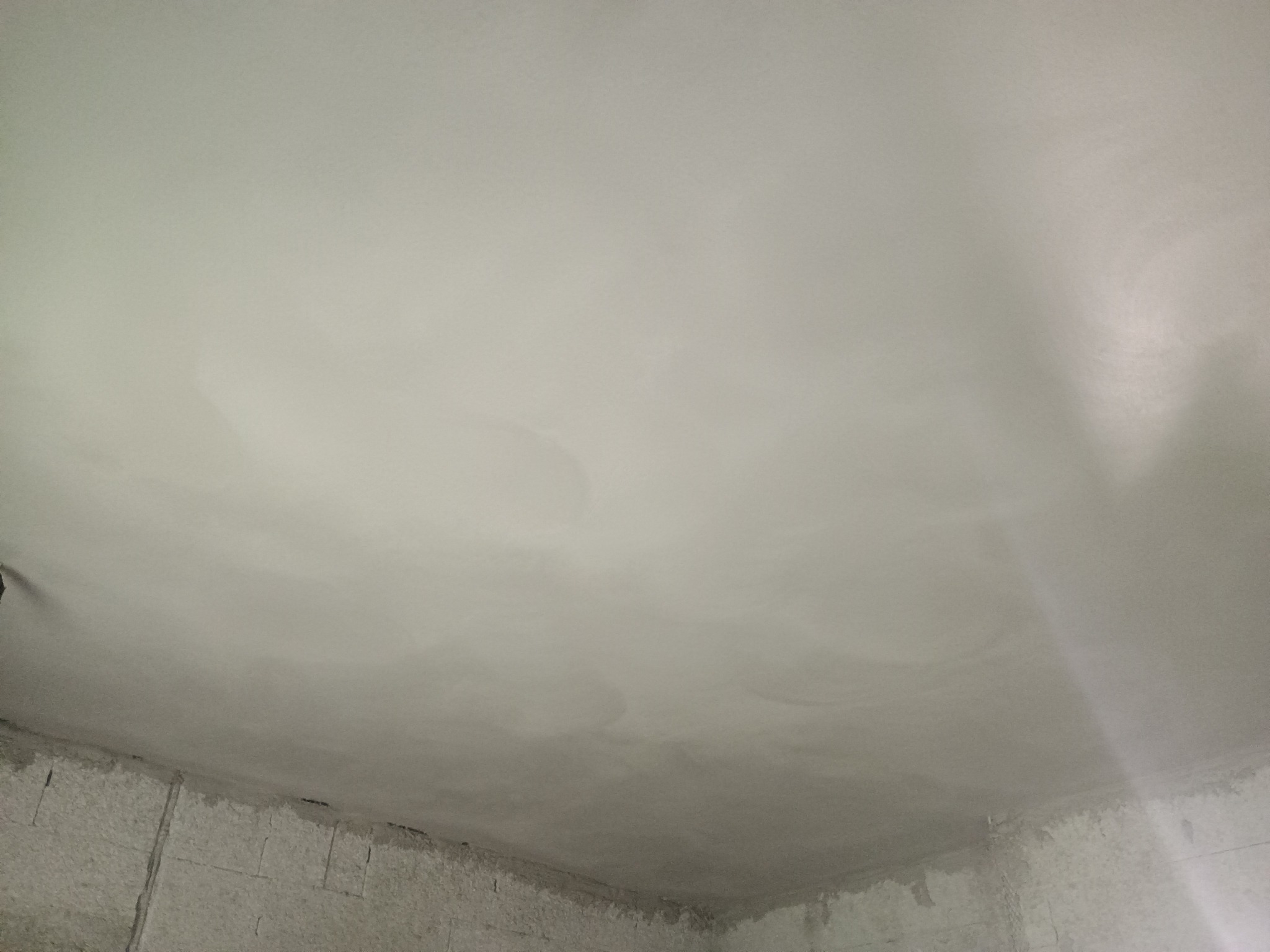 Świeżo położony, wilgotny tynk na suficie w rogu pomieszczenia, widoczna surowa ściana z bloków.