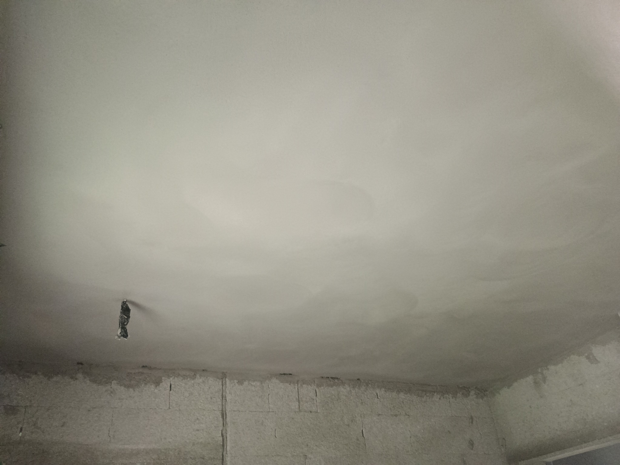 Świeżo otynkowany sufit z widocznym otworem na instalację elektryczną, ściany w stanie surowym.