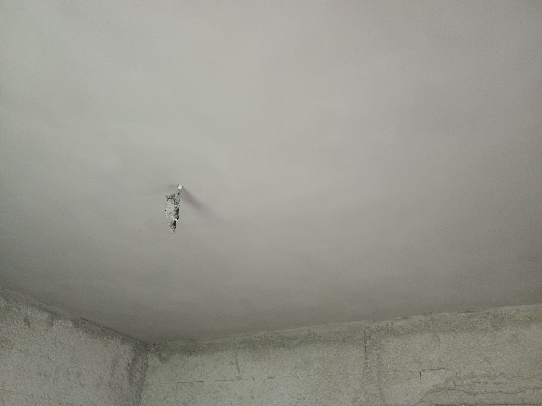 Fragment sufitu i ściany po nałożeniu tynku, widoczne nierówności i niedociągnięcia w narożniku, oraz otwór po instalacji elektrycznej.